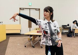 Yukie Sakaguchi rzucająca w kierunku tarczy. Japonka ubrana jest w charakterystyczny dla siebie krawat.